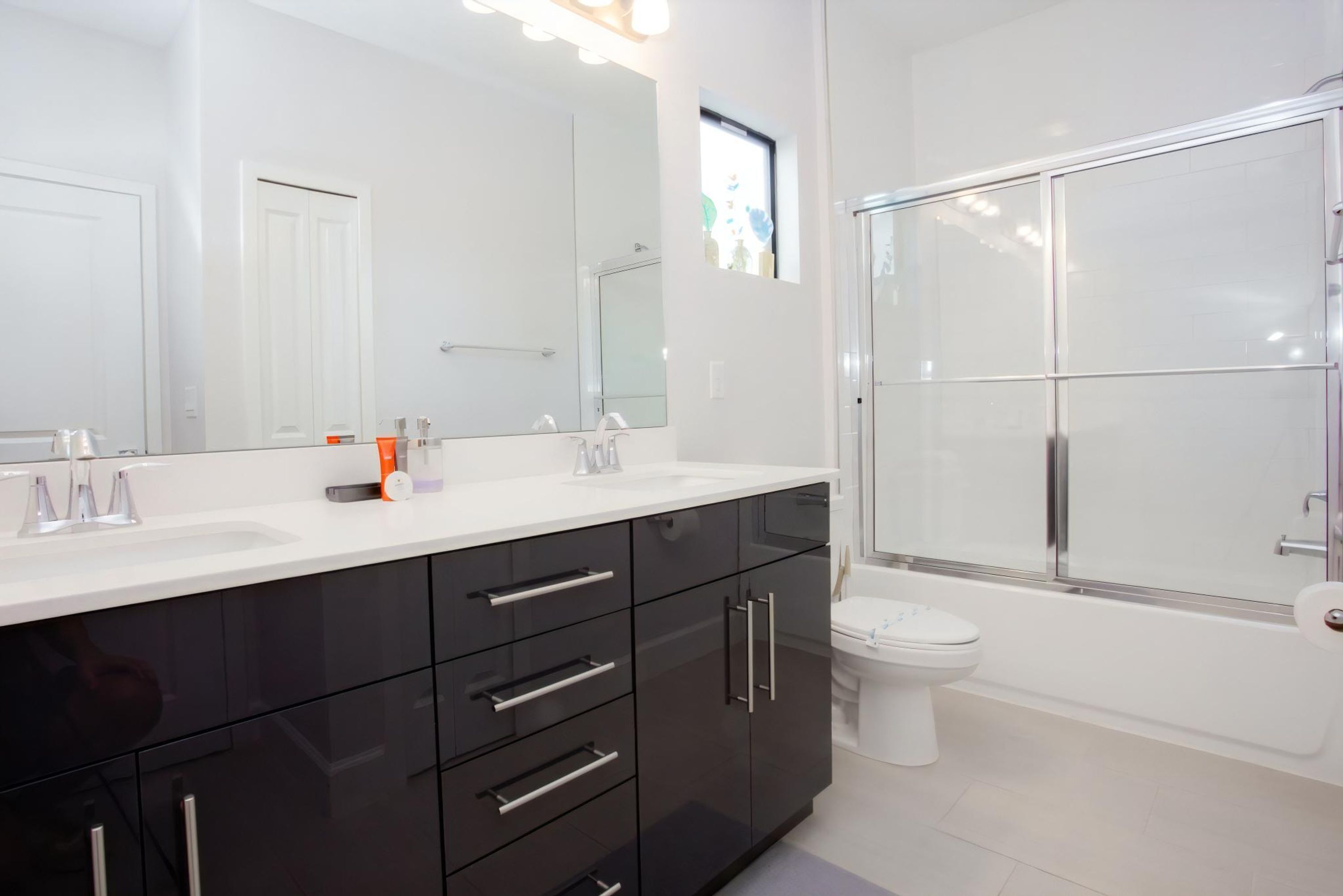 A modern bathroom with a large mirror, two sinks, a toilet, and a glass-enclosed shower.