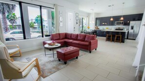 A modern living room with a sectional sofa, a coffee table, and a dining area with a kitchen in the background. - Townhome- 4Bd - Close To Parks Shops (Davenport)