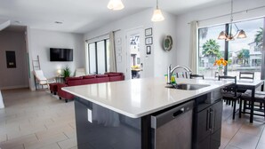 A modern kitchen with a large island, a dining area with a table and chairs, a red sofa, and a TV mounted on the wall. - Townhome- 4Bd - Close To Parks Shops (Davenport)
