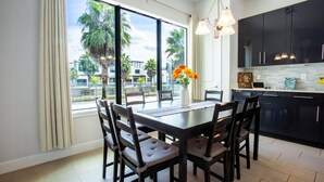 A modern kitchen with dark cabinets, a dining table with chairs, and a view of palm trees through large windows. - Townhome- 4Bd - Close To Parks Shops (Davenport)