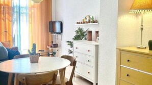 A modern living room with a round dining table, wooden chairs, a television on a stand, a white cabinet, and a lamp. - C Ntrico y Acogedor Ideal Para Explorar la Ciudad (Alicante)