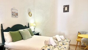A neatly made bed with a floral bedspread, a bedside lamp, and a small table with a chair. - C Ntrico y Acogedor Ideal Para Explorar la Ciudad (Alicante)