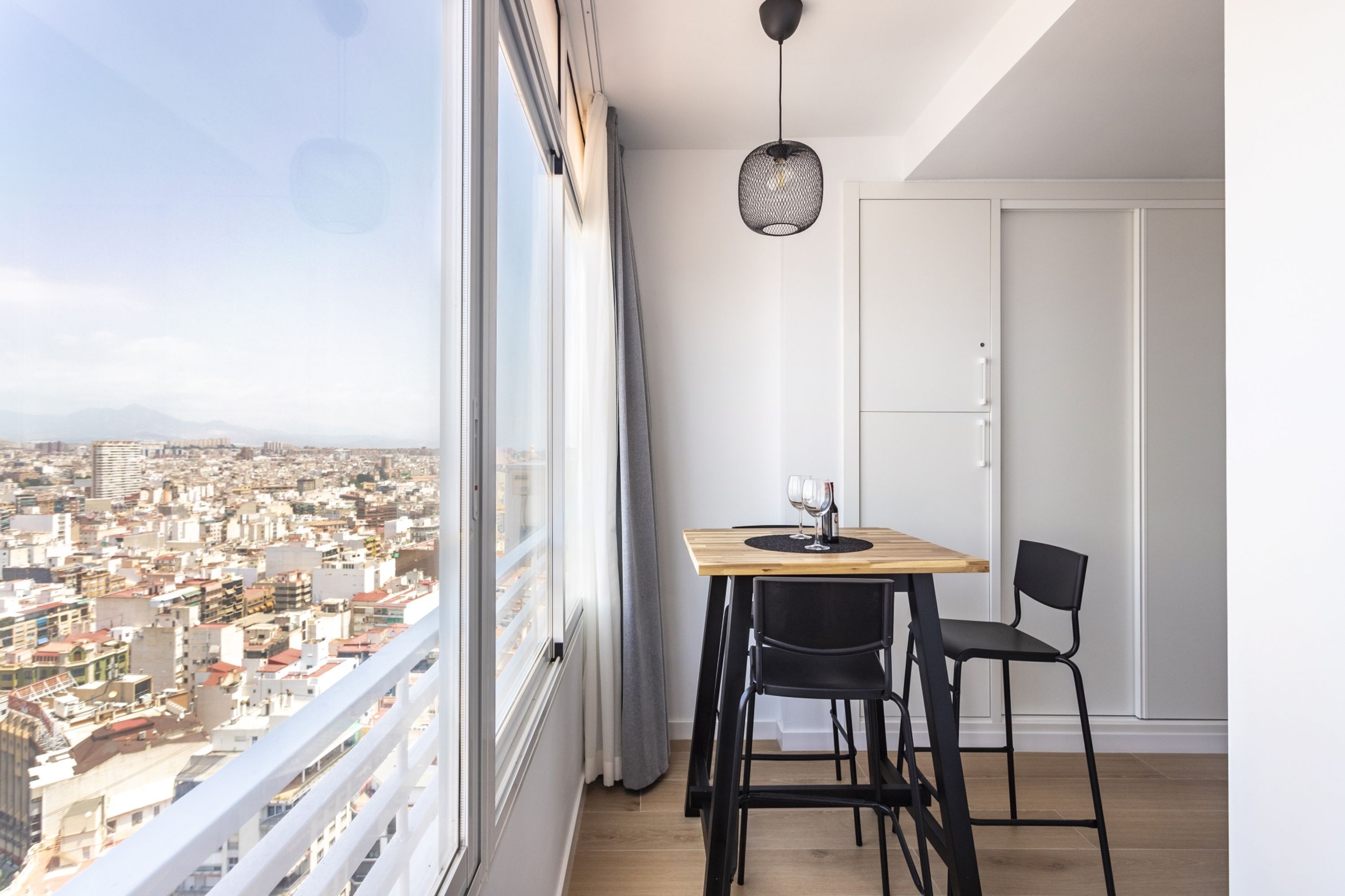 Ein Balkon mit einem Holztisch, zwei schwarzen Stühlen und einer hängenden Lampe.
