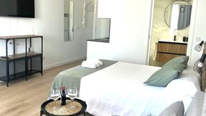 A modern hotel room with a bed, a small table with wine glasses, a TV, a mirror, and a bathroom visible through an open door. - Luxury Views Downton (Alicante)