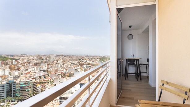 A balcony with a city view, a wooden bench, and a small dining area with chairs and a table. - Luxury Views Downton (Alicante)