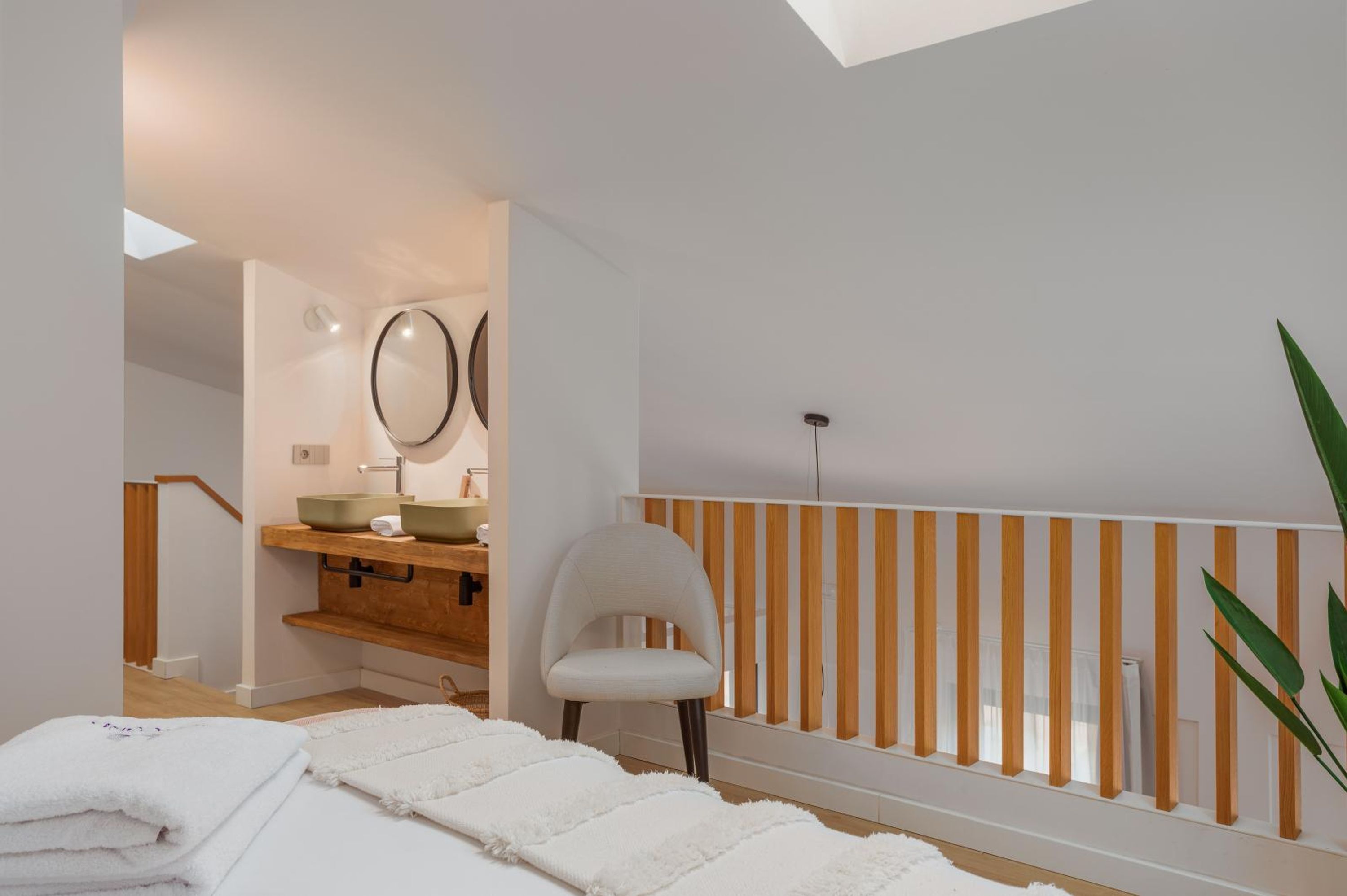 Une salle de bain moderne avec un puits de lumière, des éléments décoratifs en bois, une chaise blanche et un porte-serviettes blanc.