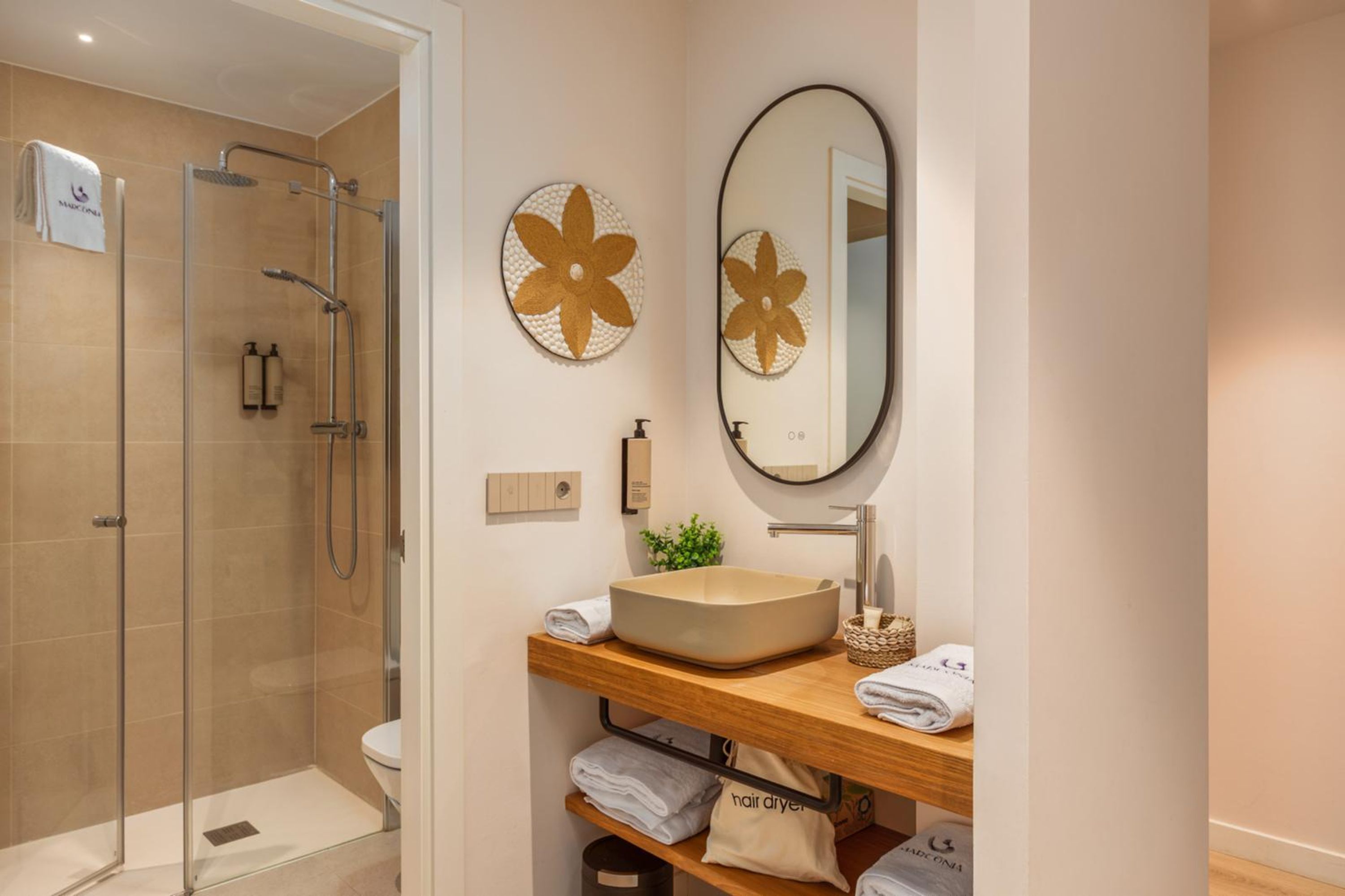 A modern bathroom with a glass-enclosed shower, a wooden vanity with a beige sink, and two wall-mounted flower-shaped mirrors.