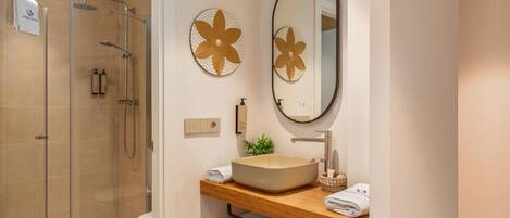 A modern bathroom with a glass-enclosed shower, a wooden vanity with a beige sink, and two wall-mounted flower-shaped mirrors.