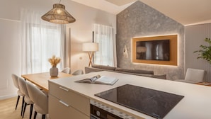 A modern kitchen with a central island, a dining area with chairs, a sofa, and a TV mounted on a textured wall.