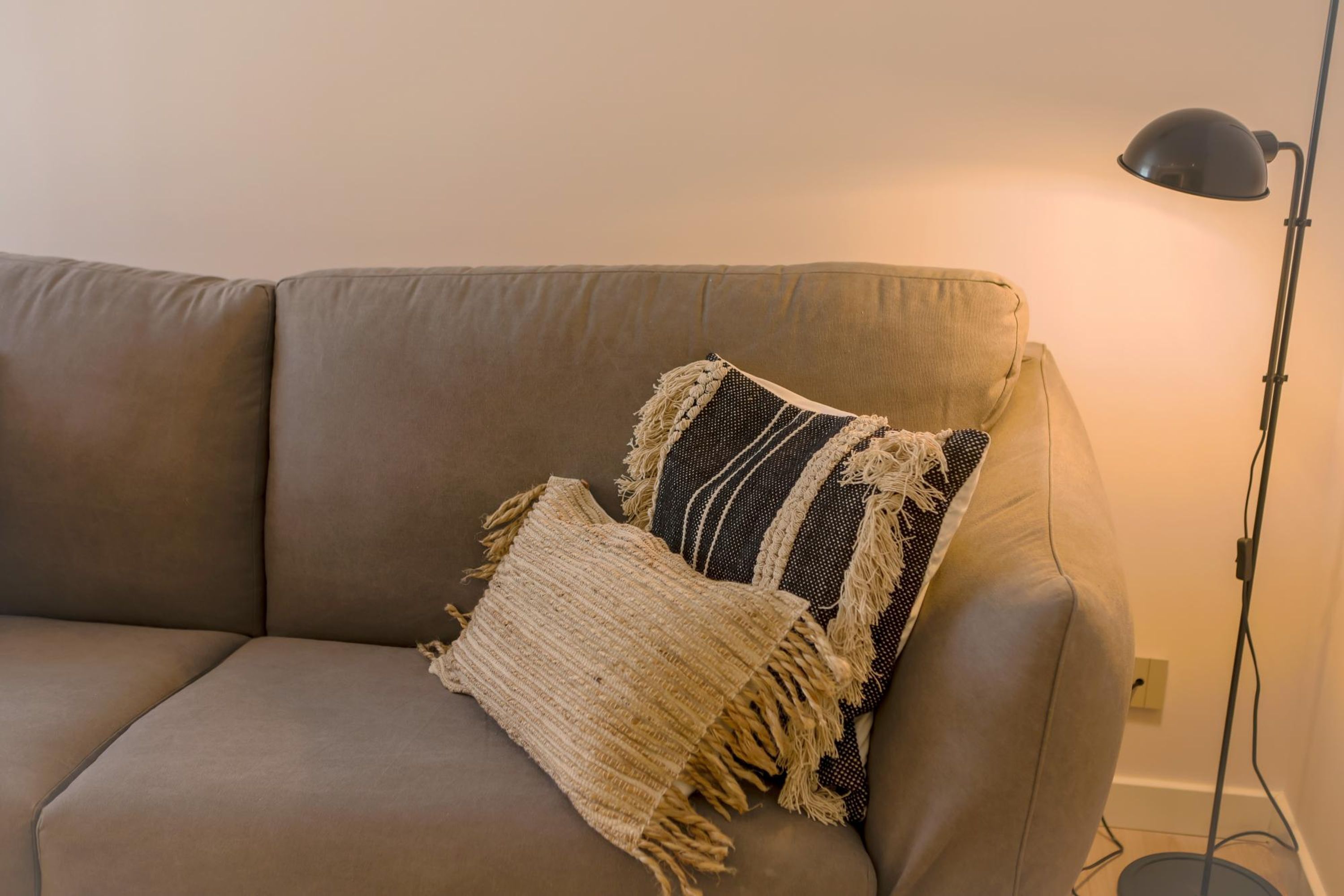 Ein beiges Sofa mit zwei Zierkissen und einer Stehlampe.