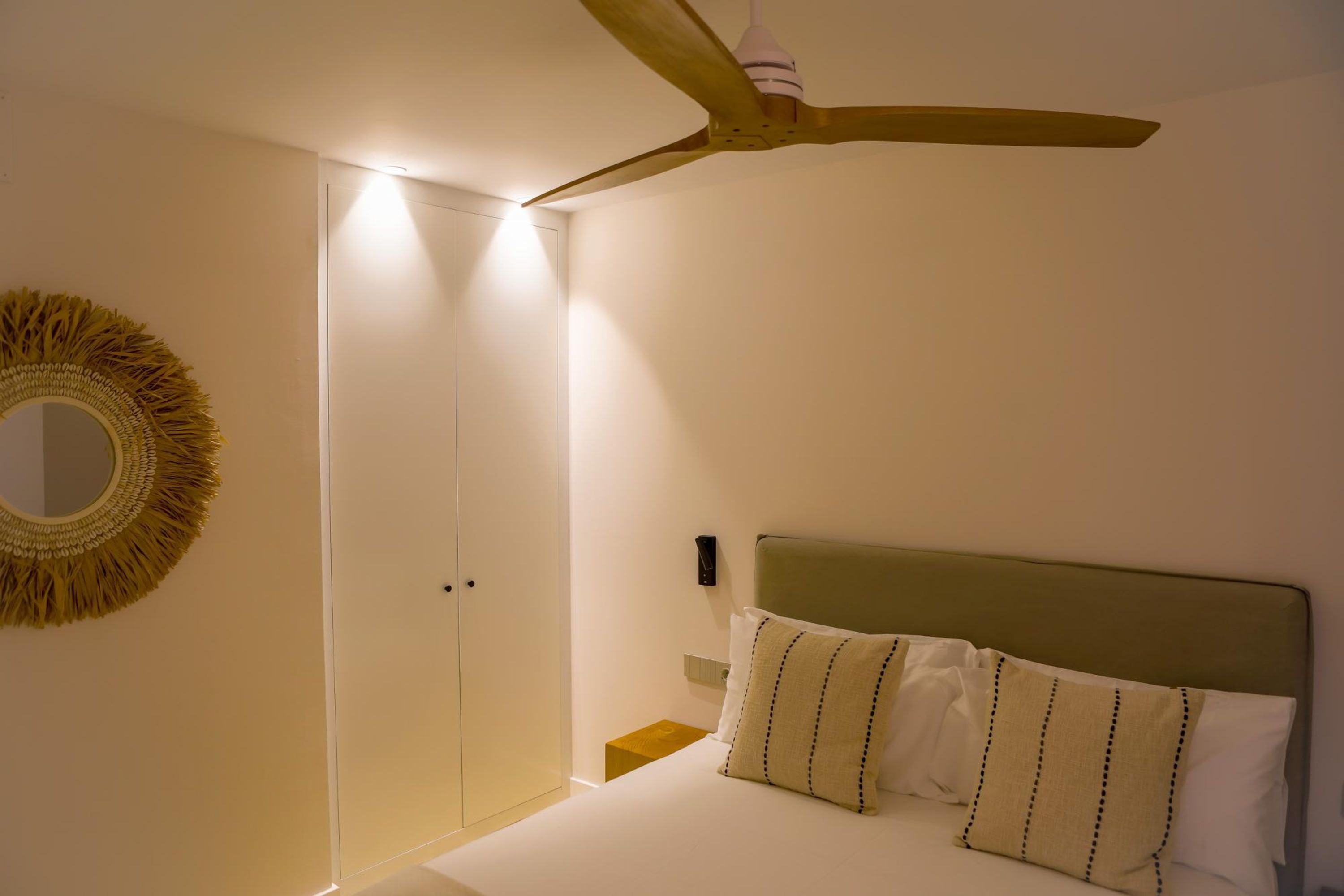 A bedroom with a bed, a ceiling fan, a wall-mounted mirror, and a door.