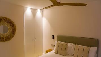 A bedroom with a bed, a ceiling fan, a wall-mounted mirror, and a door.