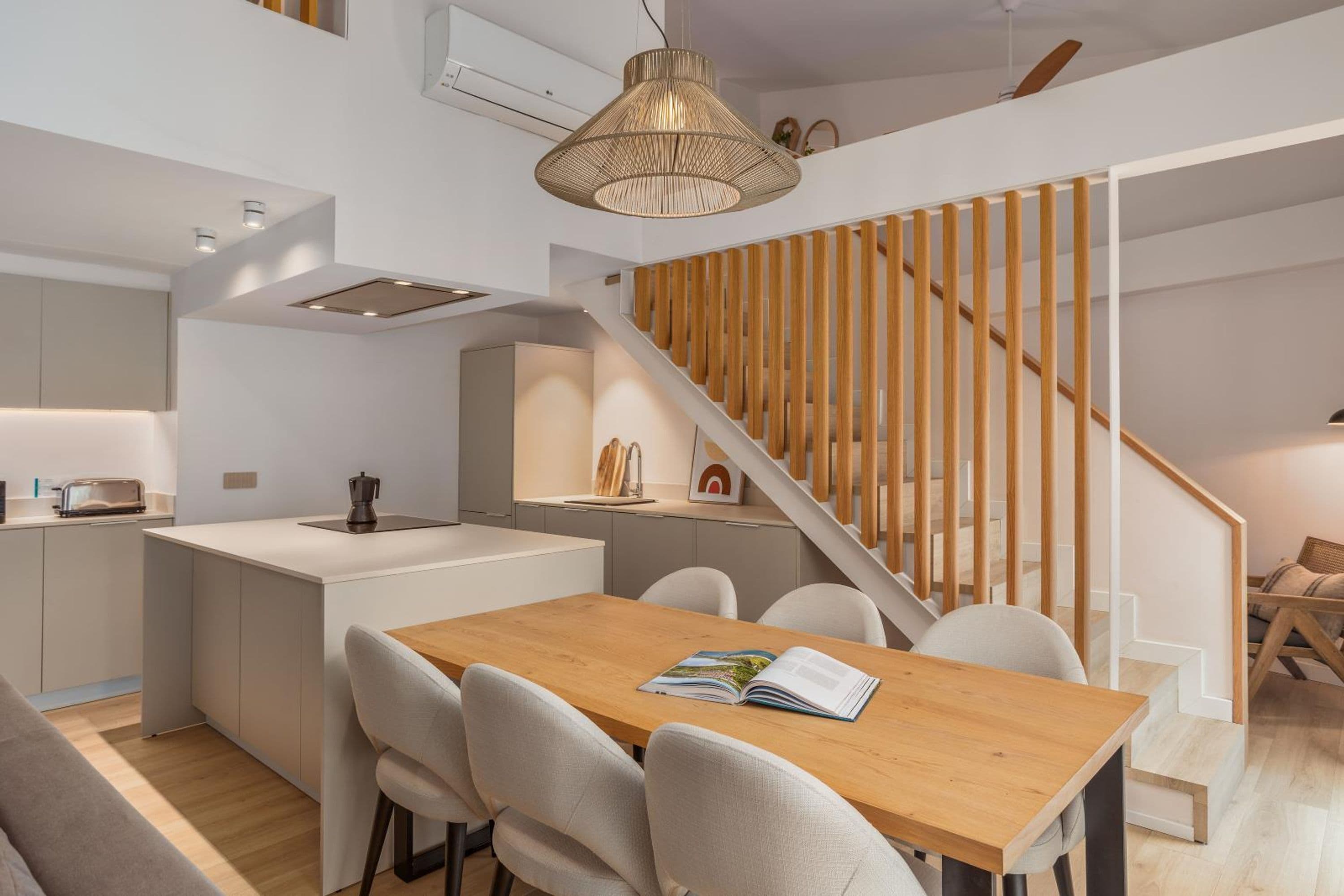 Eine moderne Küche mit einer Holztischinsel, einem Essbereich mit Holztisch und einer Treppe mit Holzbalkonen.
