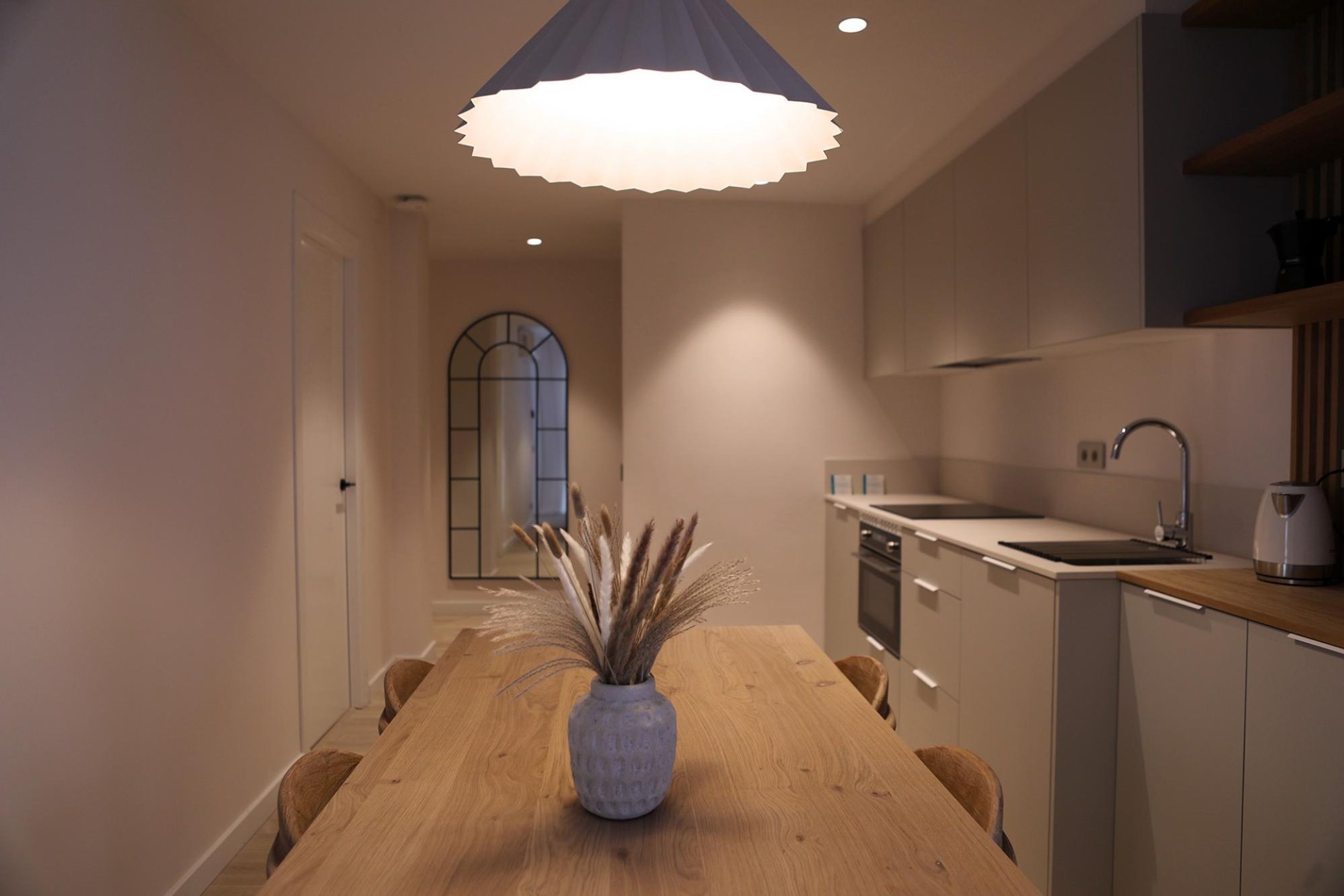 Una cocina moderna con una mesa de comedor de madera, un jarrón con plantas secas y una lámpara colgante.