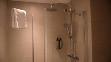 A glass-enclosed shower with a handheld showerhead, a wall-mounted towel rack, and two bottles of shampoo and conditioner.