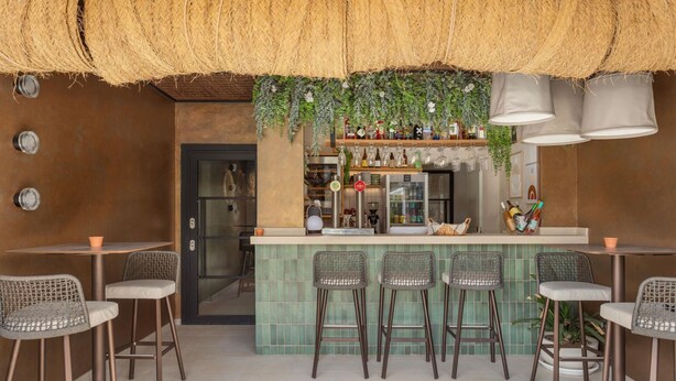 A bar area with a green tiled bar counter, wicker chairs, and hanging plants.