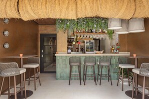Un espace bar avec un comptoir recouvert de carreaux verts, des chaises en osier et des plantes suspendues.
