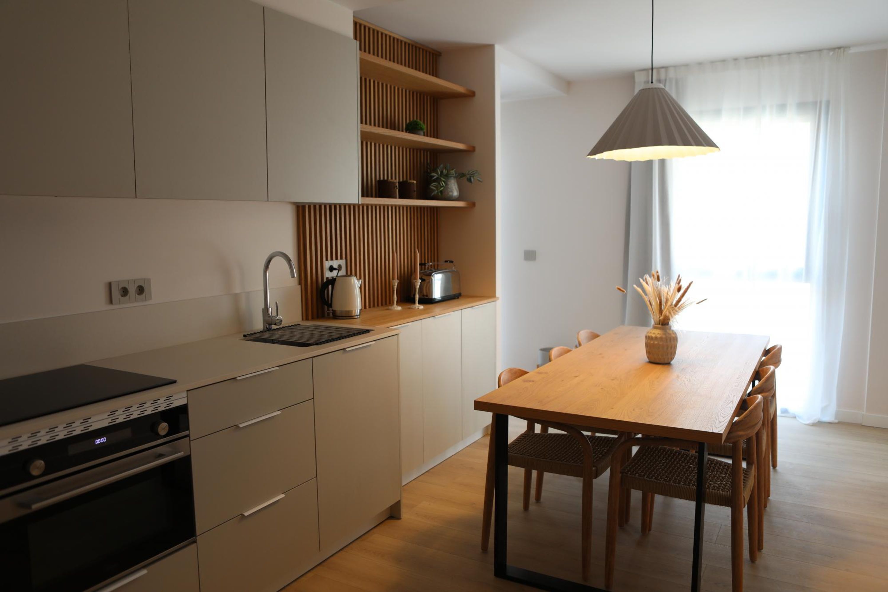 Una cocina moderna con horno empotrado, una mesa de comedor de madera con sillas y una lámpara colgante.