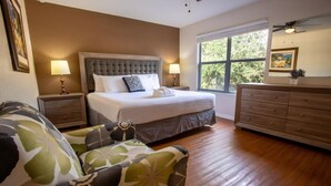 A bedroom with a large bed, two bedside tables, a dresser, a window with a view of trees, and a patterned armchair. - Where Memories Flourish 8 Mins to Disney (Davenport)