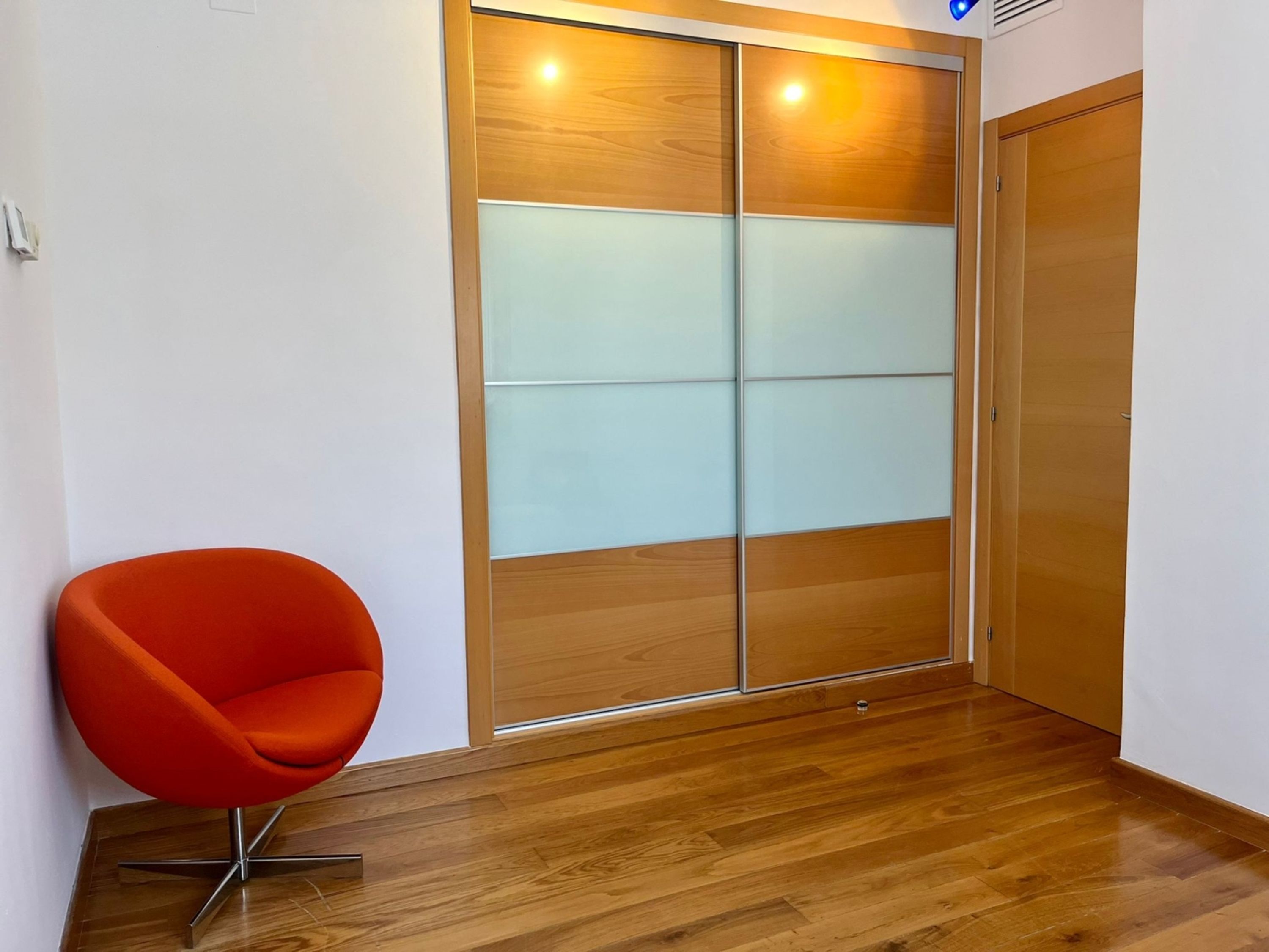 A room with a wooden floor, a sliding glass door with frosted panels, and a single orange chair.