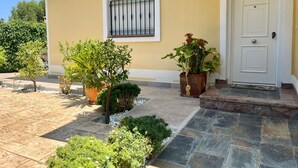 Uma casa com entrada em azulejos, janela com grades e plantas em vasos.