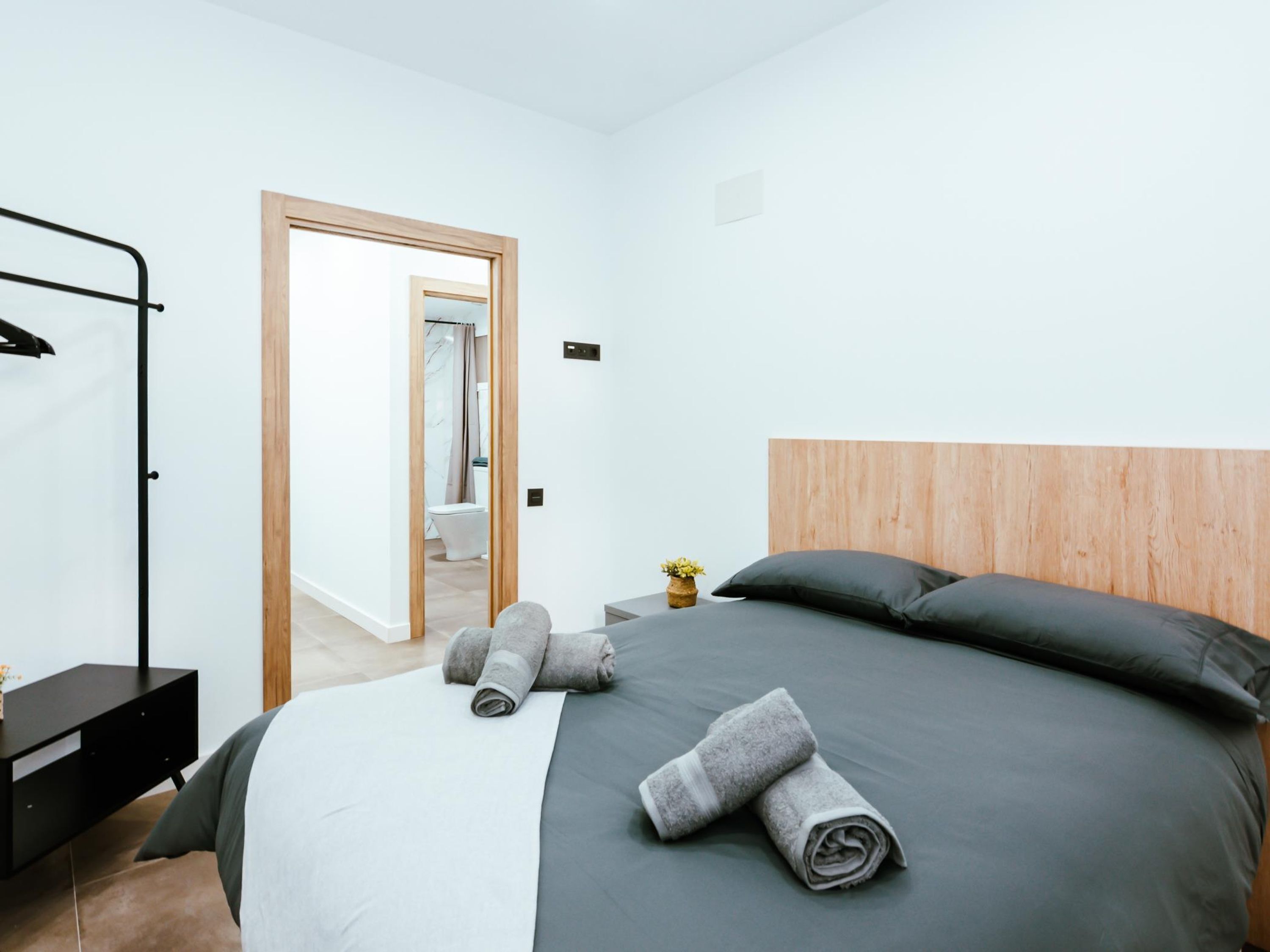 A modern bedroom with a bed, a wooden headboard, a bedside table, and a mirror.