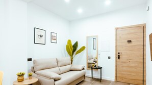 A modern living room with a beige sofa, a small round table with a plant, a mirror, and a wooden door.