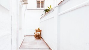 A narrow, white-walled corridor with a tiled floor leading to a small seating area with a table and chairs.
