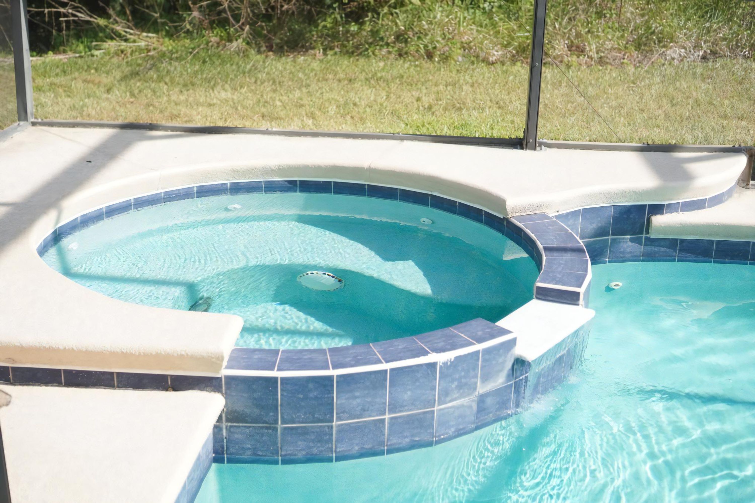 A swimming pool with a hot tub area, surrounded by a tiled deck.