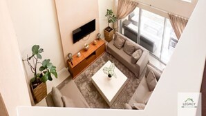 A modern living room with a flat-screen TV, a sofa, a coffee table, and a large window offering a view of the outdoors.