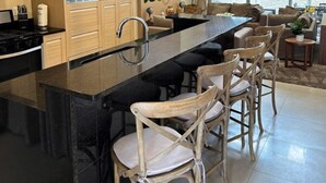 A modern kitchen with a central island, wooden cabinets, a microwave, and a dining area with wicker chairs.