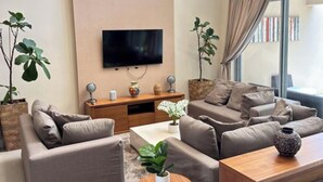 A modern living room with a flat-screen TV mounted on the wall, a wooden coffee table, two sofas, and a small round table with a plant.