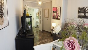 A hotel lobby with a marble floor, a black console table with a television, a white chair, a table with a pink rose, and a framed photo on the wall. - Bonito Apartamento en Centro Ciudad con Garaje (Albaida)