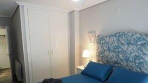 A bedroom with a bed, a wardrobe, a nightstand with a lamp, and a wall with a floral pattern. - Bonito Apartamento en Centro Ciudad con Garaje (Albaida)