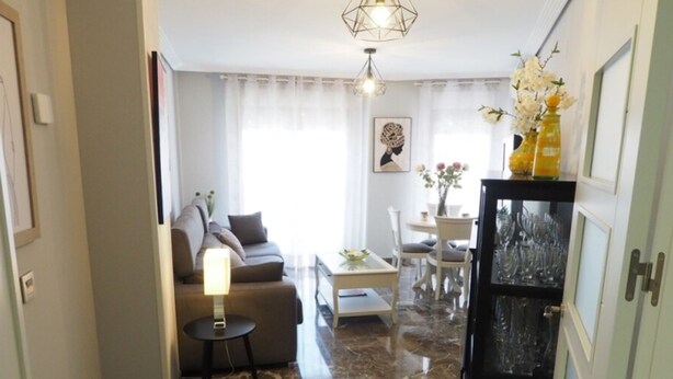 A modern living room with a sofa, a coffee table, and a dining area with chairs. There is a glass cabinet with decorative items. - Bonito Apartamento en Centro Ciudad con Garaje (Albaida)