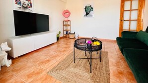 Una sala de estar con una televisión de pantalla plana, un sofá verde, una mesa de centro con frutas y un elemento decorativo en la pared.