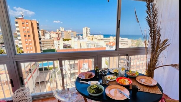 Un balcón con una mesa dispuesta para una comida, con vistas a la ciudad y al mar.
