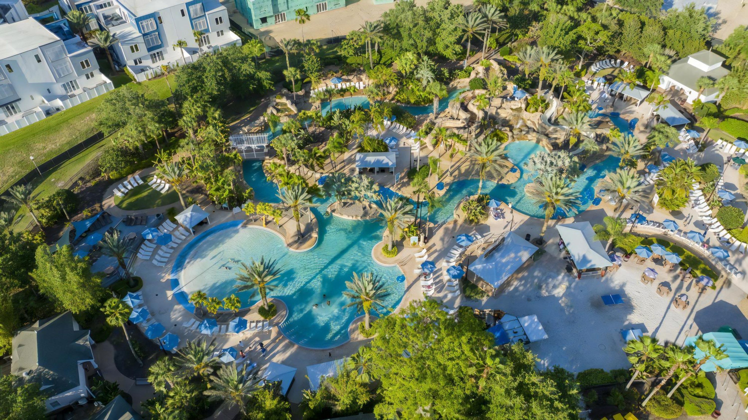 An aerial view of a resort with multiple swimming pools, lounge areas, and palm trees.