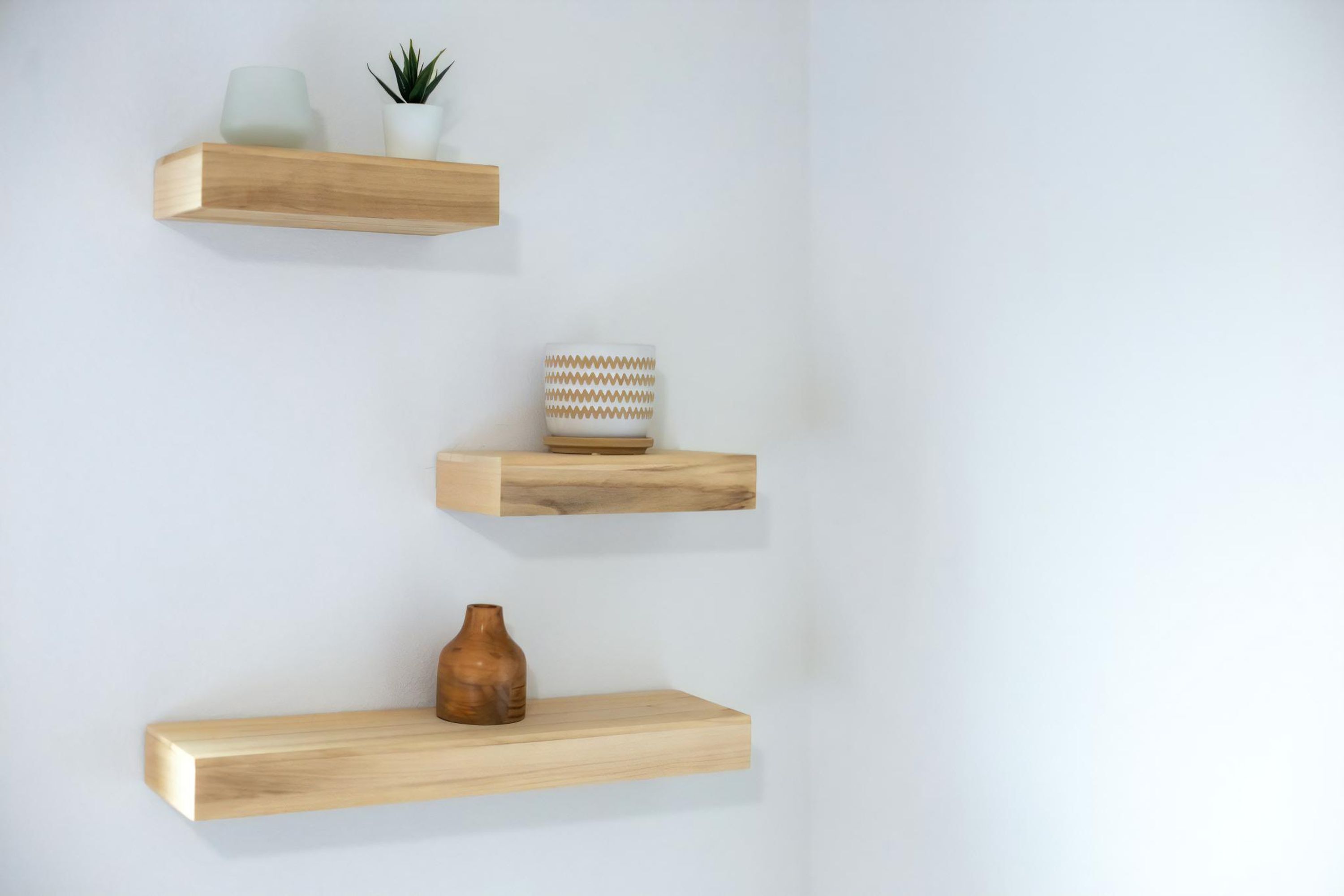 Three wooden shelves against a white wall, each holding different items.