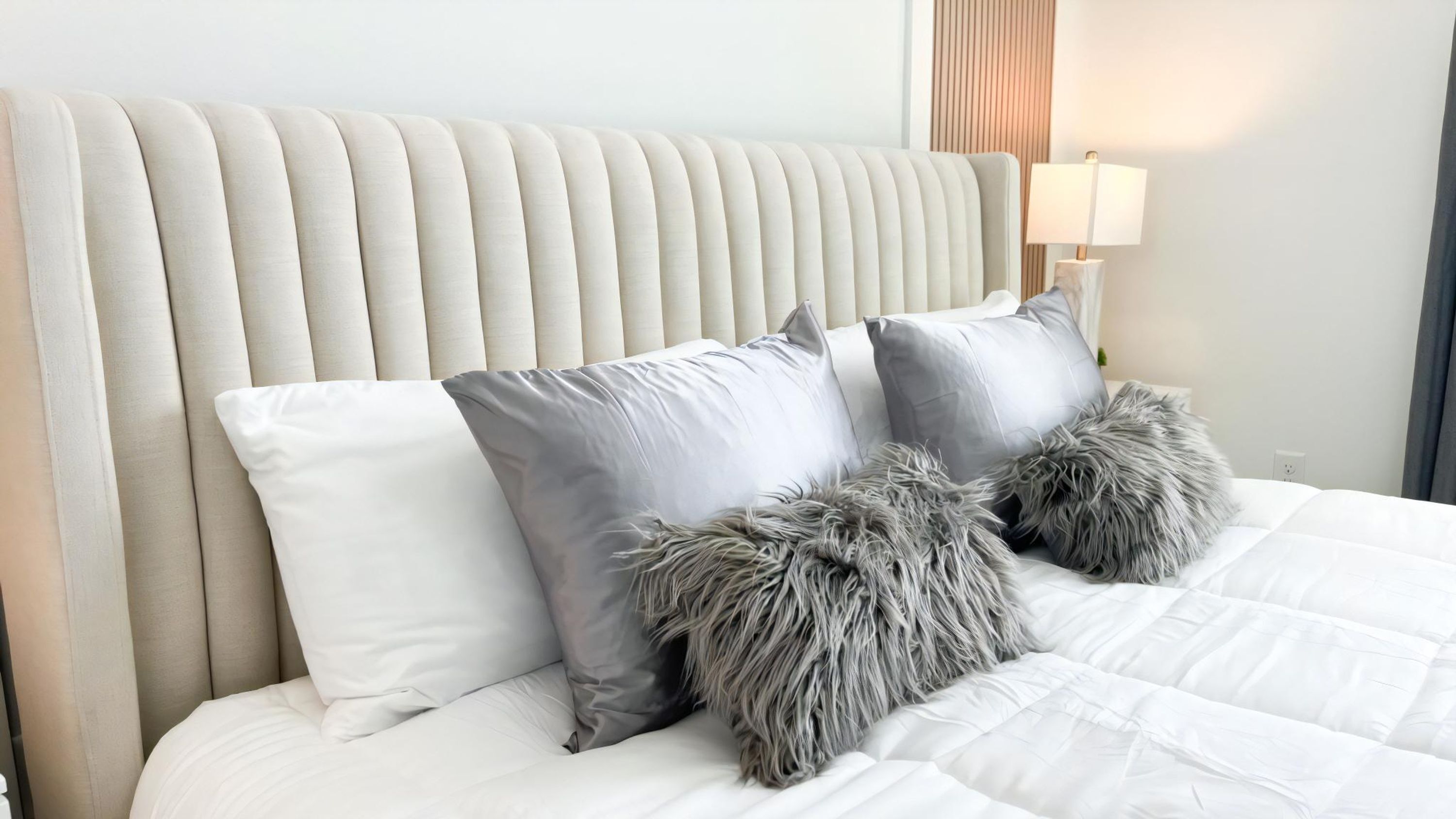 Una cama con cabecera capitonada, almohadas grises y blancas, y almohadones grises suaves.