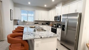 A modern kitchen with white cabinets, a stainless steel refrigerator, a built-in oven, and a marble countertop. - Solara Dreams 4BD Pool Home Next to Disney (Kissimmee)
