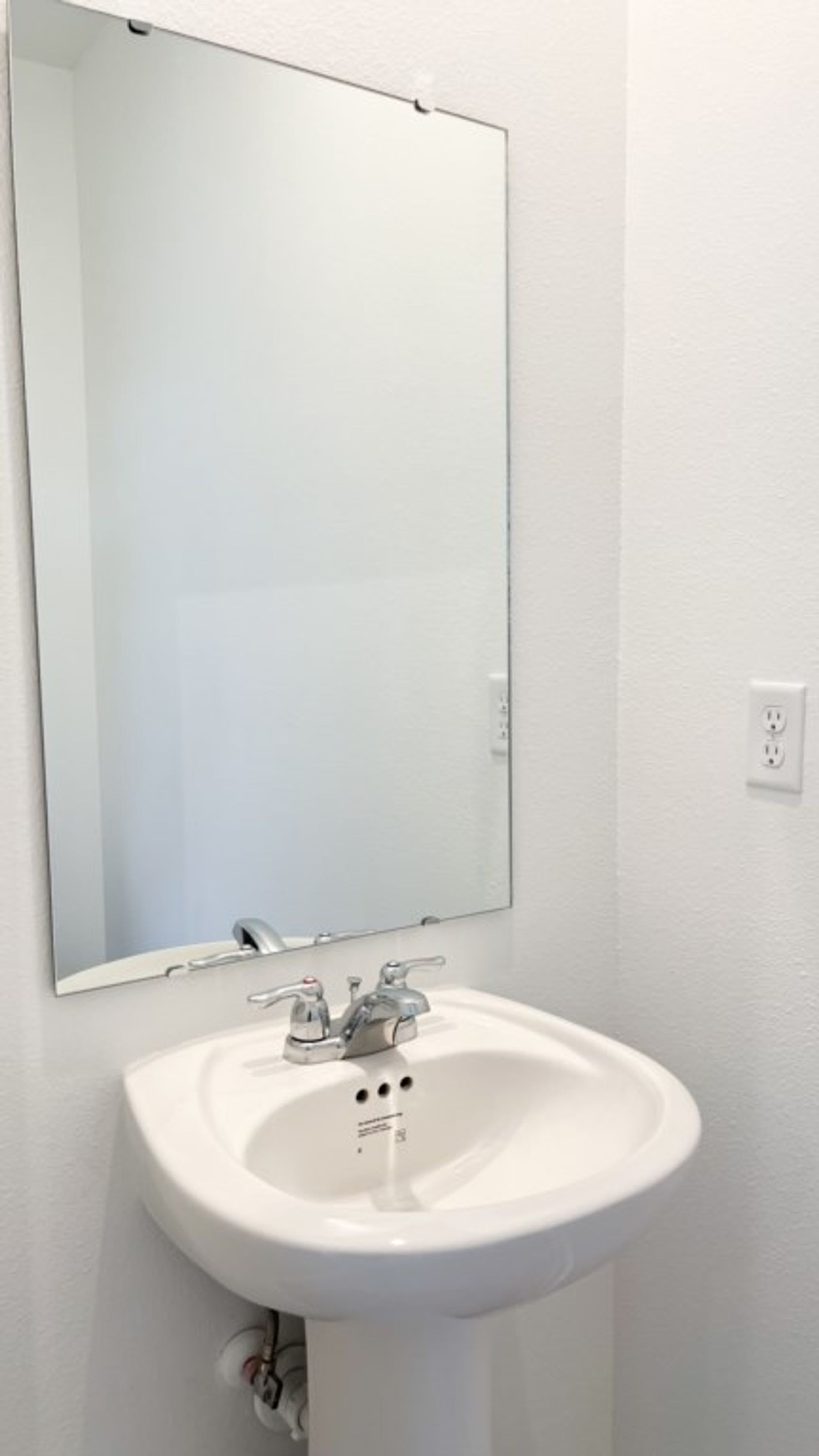 Une salle de bain blanche avec un lavabo, un miroir et une prise électrique.