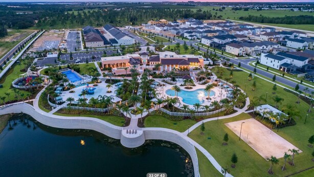 An aerial view of a residential area with a large swimming pool, multiple houses, and a well-maintained lawn. - Solara Dreams 4BD Pool Home Next to Disney (Kissimmee)