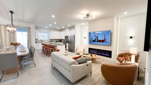 A modern kitchen with white cabinets, a large refrigerator, and a dining area with a table set for four. - Solara Dreams 4BD Pool Home Next to Disney (Kissimmee)