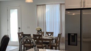 A dining area with a table and chairs, a refrigerator, and a window with curtains.