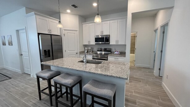 A modern kitchen with white cabinets, stainless steel appliances, granite countertops, and a central island with bar stools.