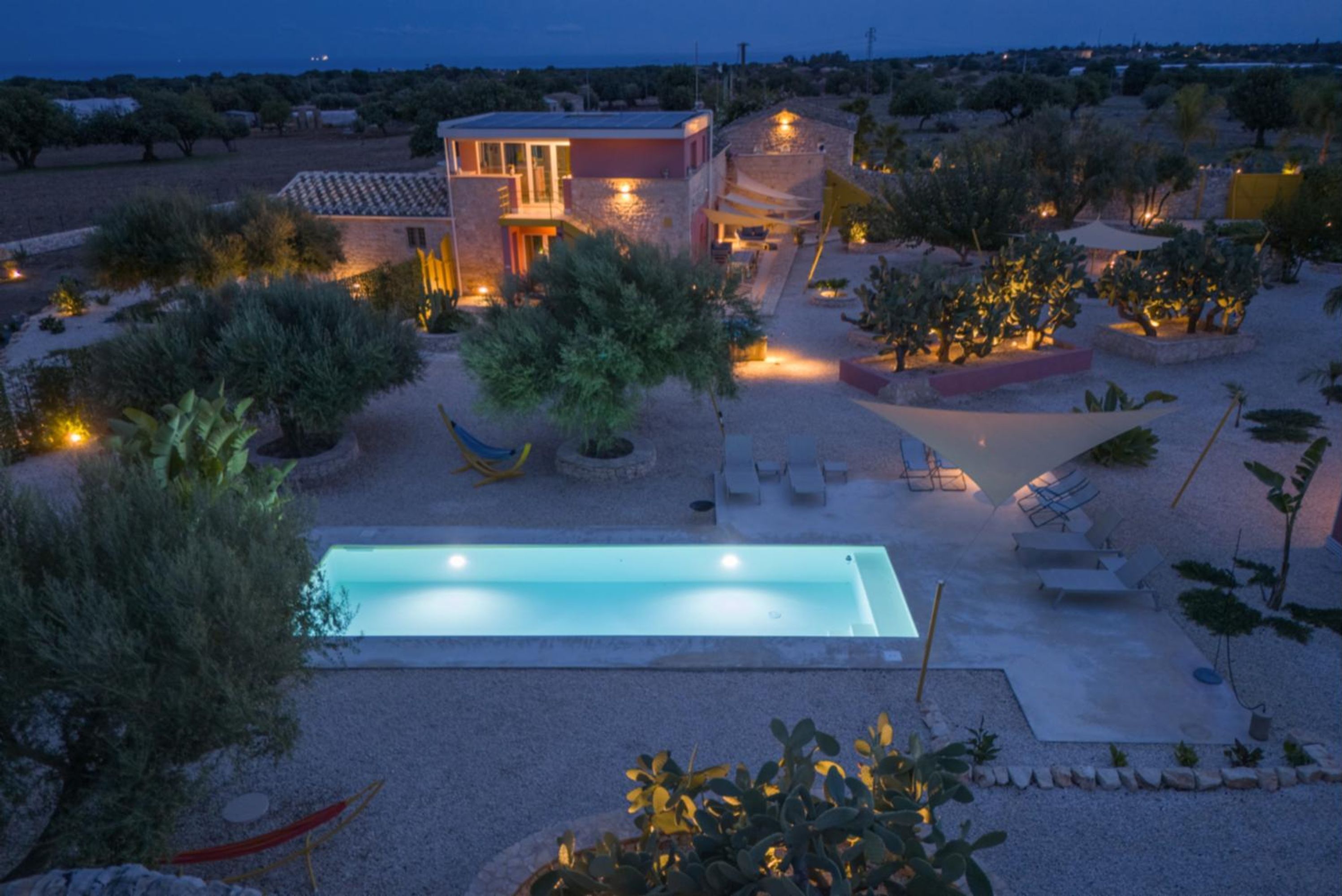 Ein modernes Haus mit Schwimmbad, Sitzgelegenheiten im Freien und einem gut beleuchteten Garten.