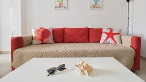 Un salon avec un canapé beige, des coussins rouges et deux œuvres d’art représentant des cactus, encadrées et accrochées au mur.