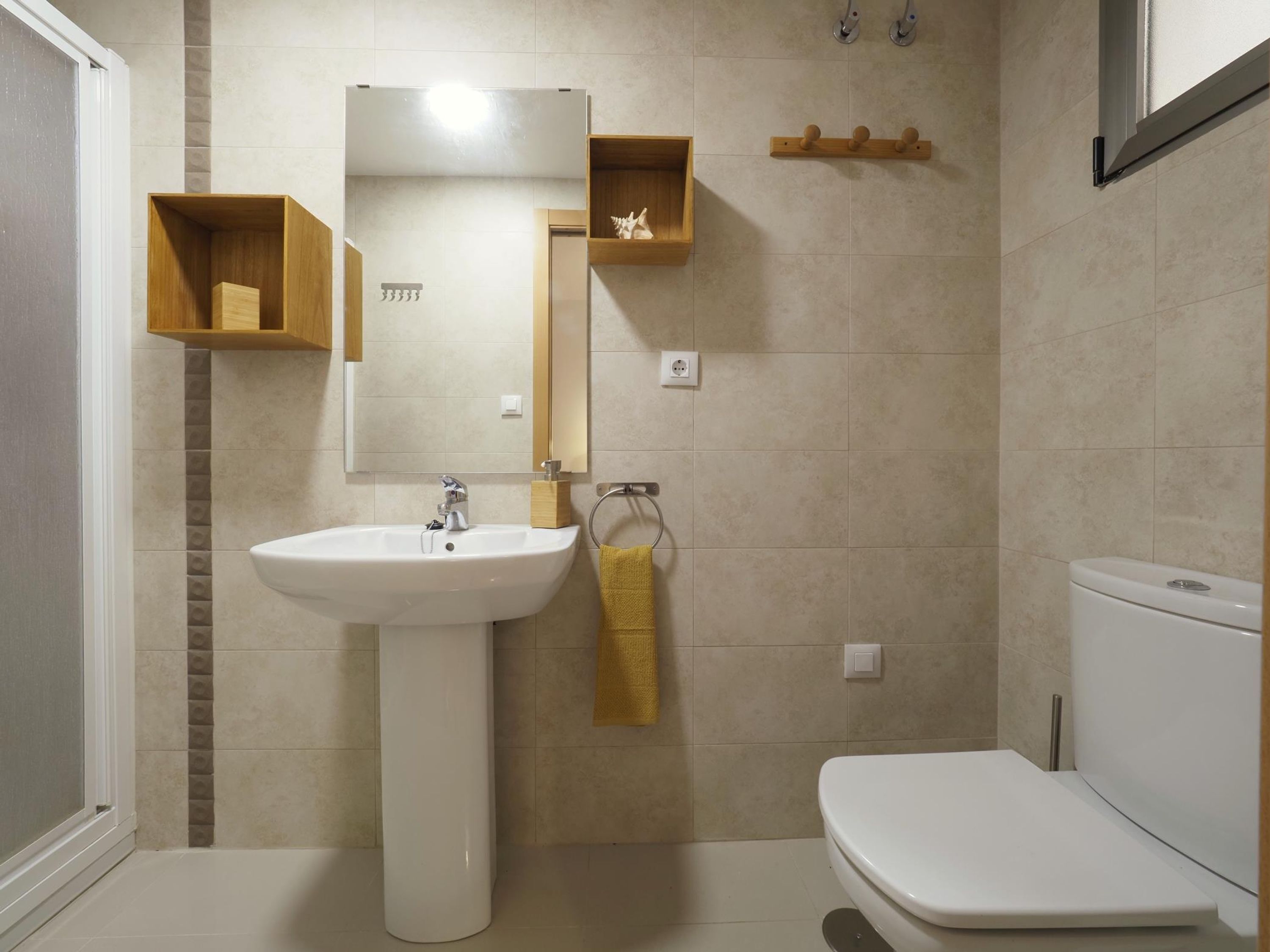 Une salle de bain avec un lavabo sur colonne, un miroir, des toilettes et une étagère sur laquelle est posée une serviette.