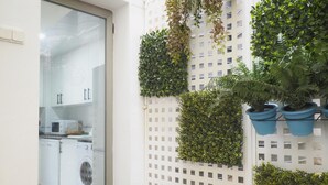 Une cuisine avec des meubles blancs, un four à micro-ondes et un lave-linge. On y trouve une chaise en bois et une table sur laquelle est posée une plante en pot.